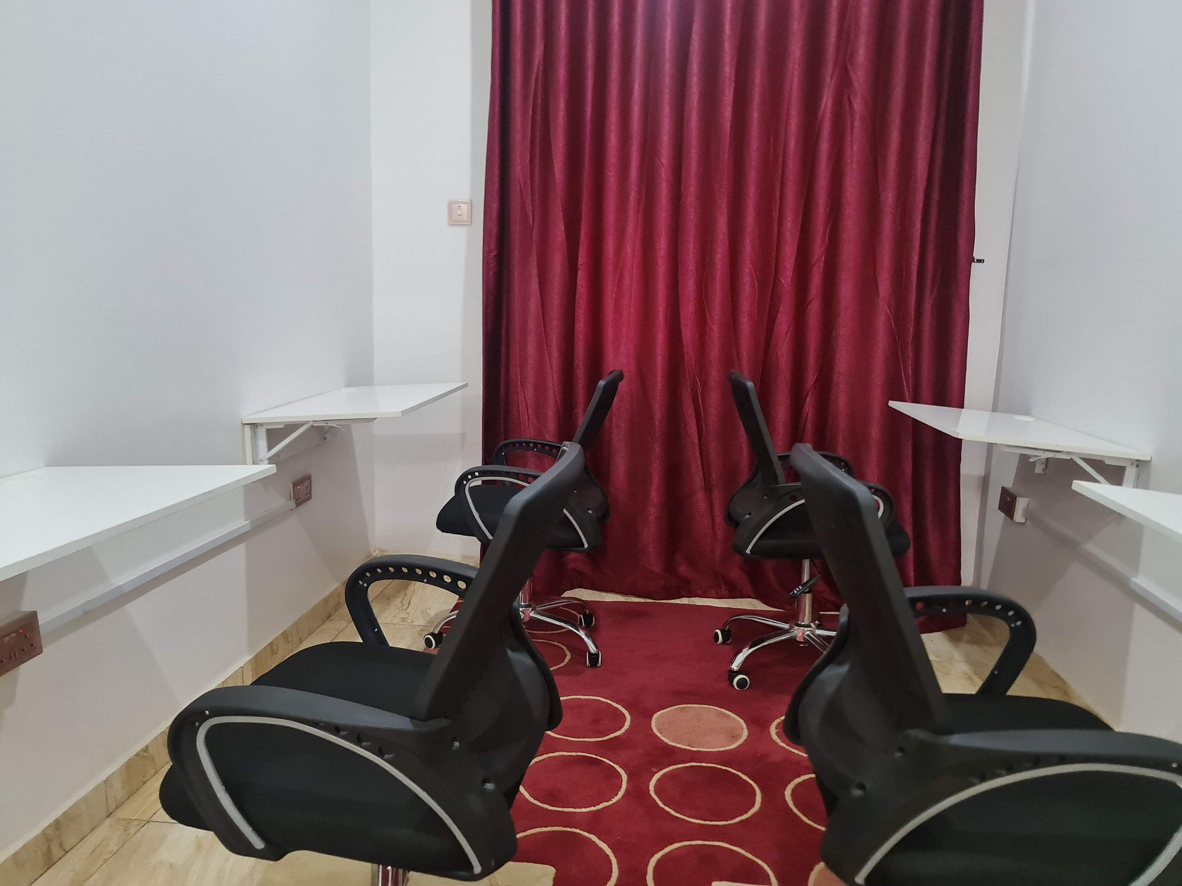 A room with four black office chairs, a red curtain, white walls, and a red carpet with circular patterns.