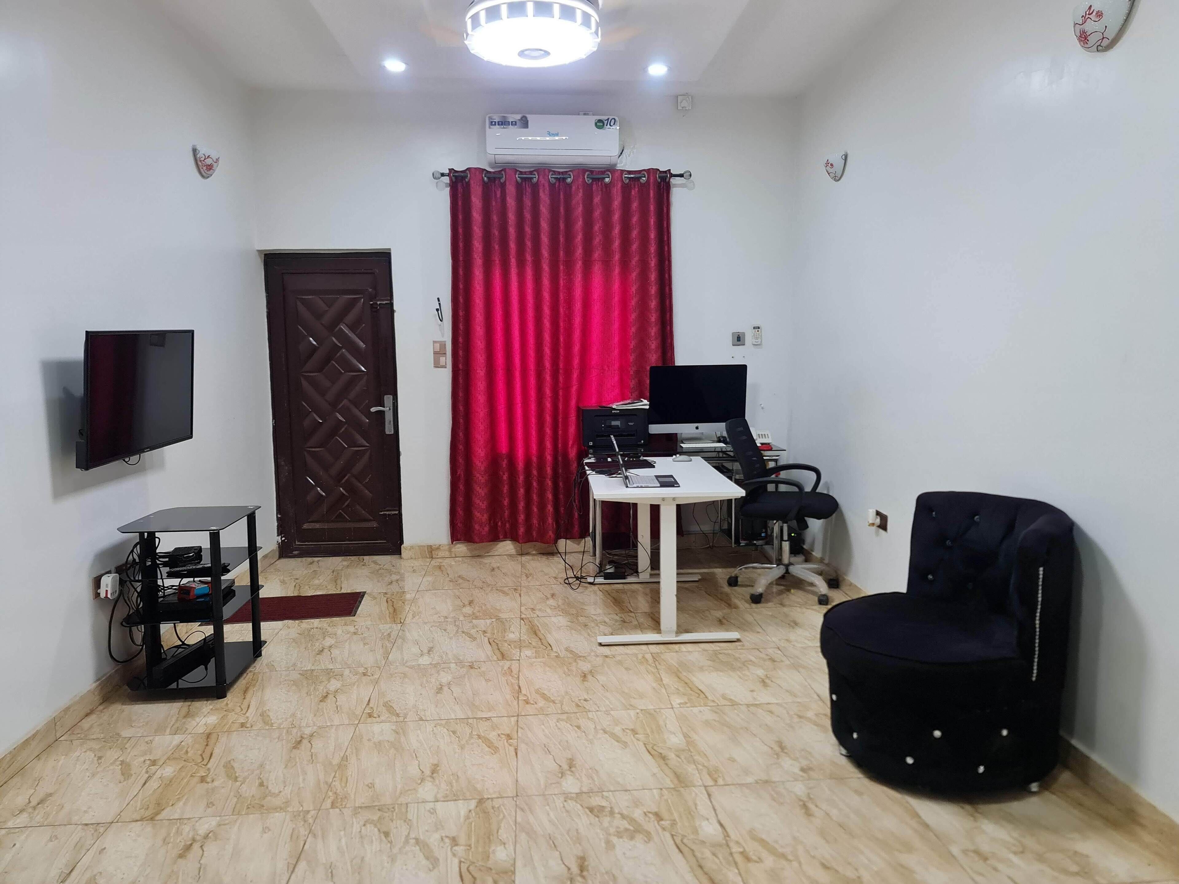 Un salon avec un téléviseur, un bureau d’ordinateur, une chaise et un rideau rouge.