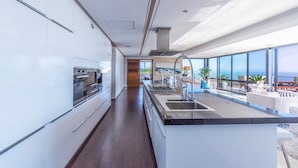 Une cuisine moderne dotée d’un îlot central, de grandes fenêtres et offrant une vue sur la mer.