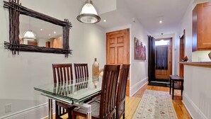 A dining area with a glass table, wooden chairs, a hanging pendant light, and a wooden door in the background. - Luxury Quiet Old Montreal Home (Montréal)