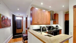 A modern kitchen with wooden cabinets, a central island with a sink, and a built-in stove. - Luxury Quiet Old Montreal Home (Montréal)