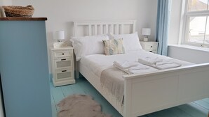 Una camera da letto ordinata con un letto bianco, due comodini, un tappeto piccolo e una finestra con tende.