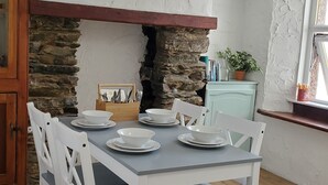 Zona pranzo con parete in pietra, sedie bianche, tavolo apparecchiato e lampadario.