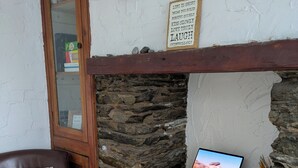 Una stanza con parete in pietra, una porta in legno, un laptop su un tavolo bianco, una poltrona in pelle marrone e un cartello con consigli di vita.