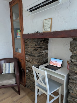 A room with a stone wall, a wooden door, a laptop on a white table, a brown leather chair, and a sign with life advice.