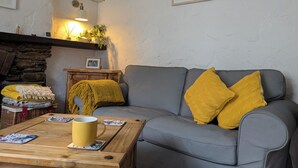 Un accogliente soggiorno con un divano grigio, cuscini gialli, un tavolino in legno con una tazza gialla, un caminetto in pietra e un quadro appeso al muro.