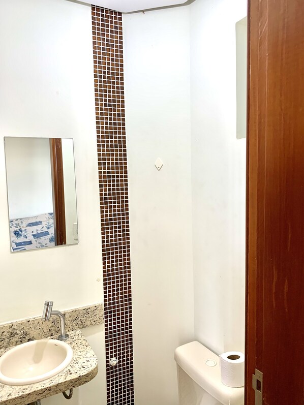 A bathroom with a white sink, a mirror, a toilet, and a shower area. - Flats Bela Vista Marista (Goiânia)