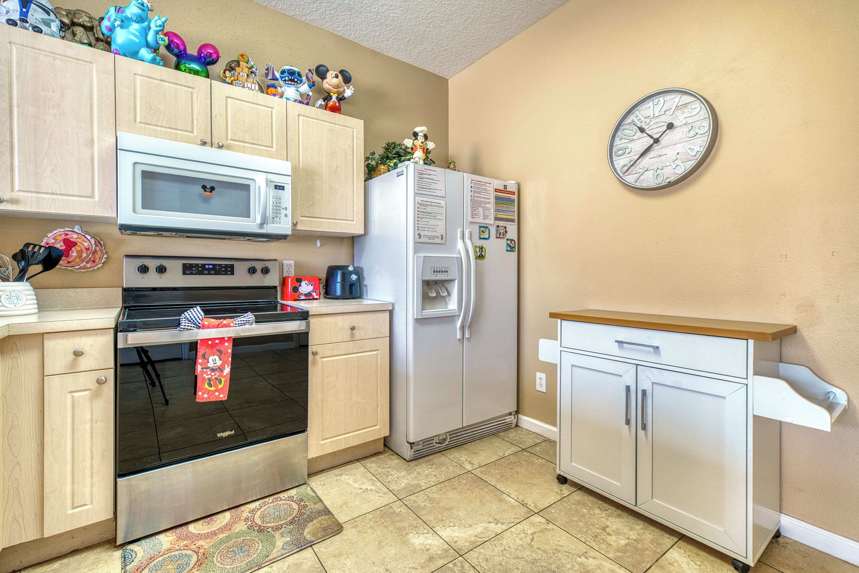 A kitchen with a microwave, oven, refrigerator, and a clock on the wall.