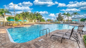 Ein Swimmingpool mit Liegestühlen und Sonnenschirmen, umgeben von Palmen und wolkenlosem Himmel.