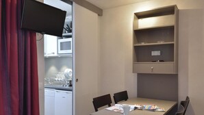 Ein gemütlicher Raum mit Esstisch, Stühlen, einem an der Wand befestigten Fernseher und einer Küchenzeile inklusive Geschirrspüler und Mikrowelle.