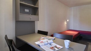 Ein kleiner, moderner Raum mit Tisch, Stühlen, einem roten Bett und einem Regal mit Steckdose.