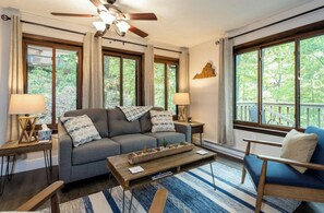 Relax in this stylish living room with a large sofa, coffee table, and armchair, offering a view of the outdoors.