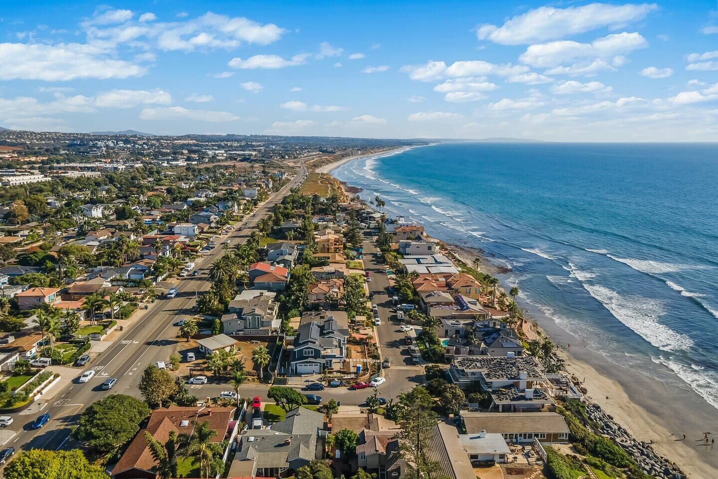 A coastal residential area with houses along the beachfront, a clear sky, and a view of the ocean.