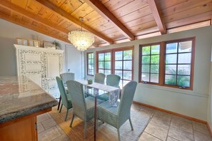 Uma área de refeições com mesa de vidro, cadeiras de vime e um candelabro.