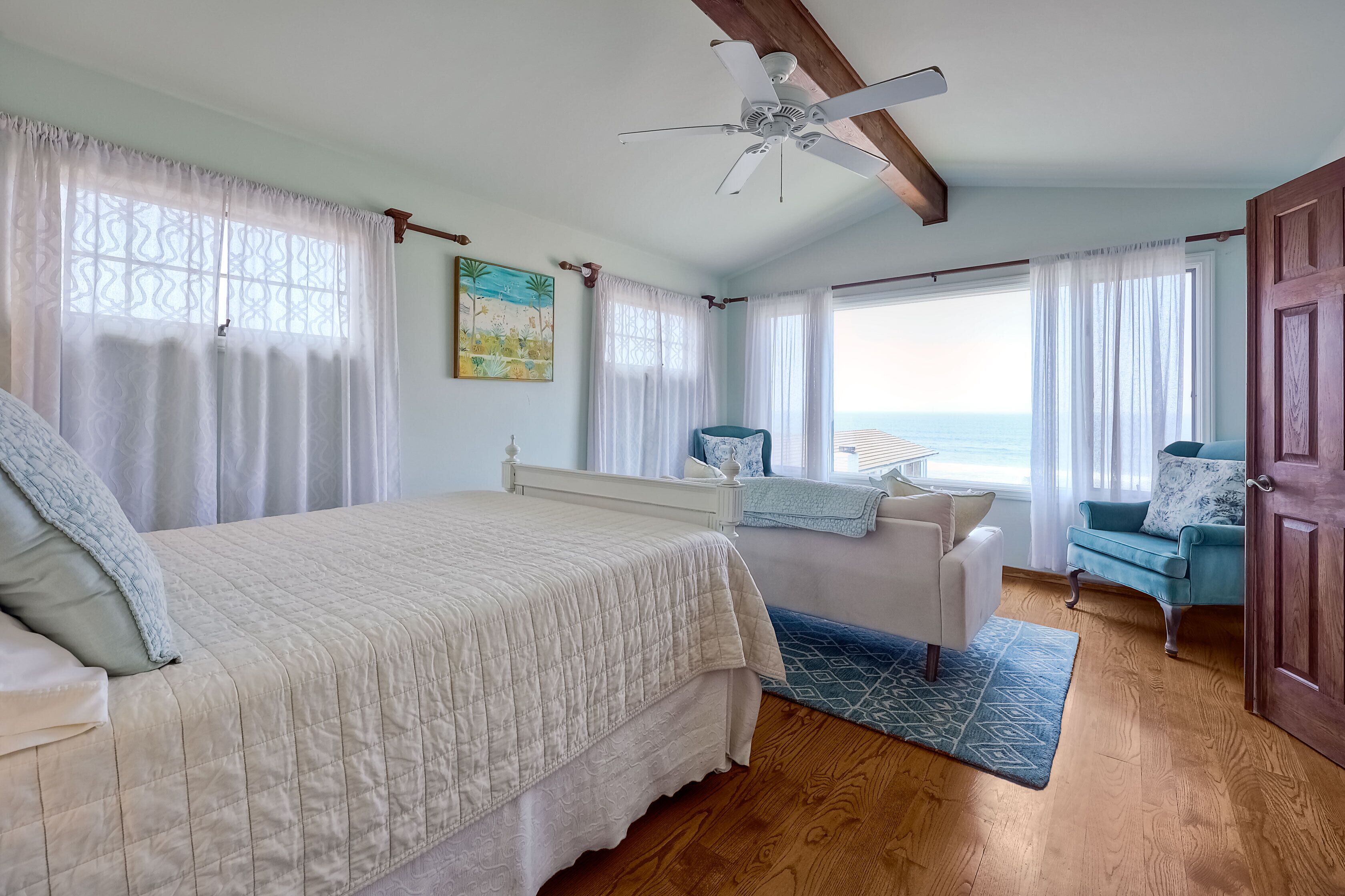 Un dormitorio con cama, una silla, un escritorio y vistas al océano.