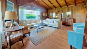 Amplia sala de estar con techo alto, paredes de madera, un ventanal grande y un rincón de descanso acogedor con un sofá blanco y sillones azules.