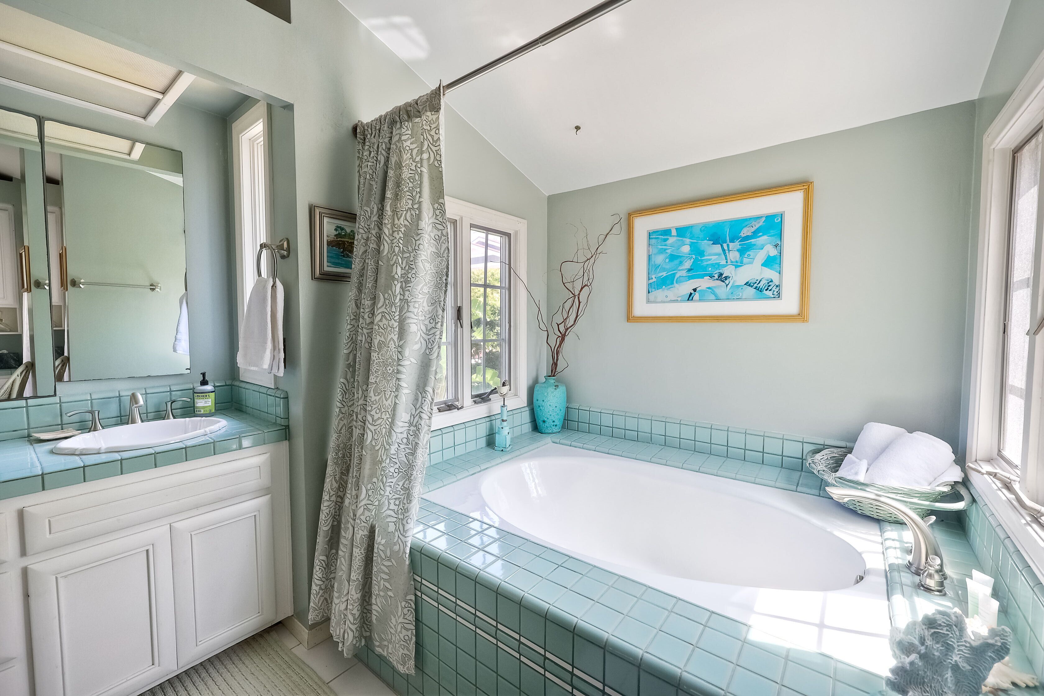 A bathroom with a large bathtub, a double sink vanity, a mirror, and a window with a view of greenery.