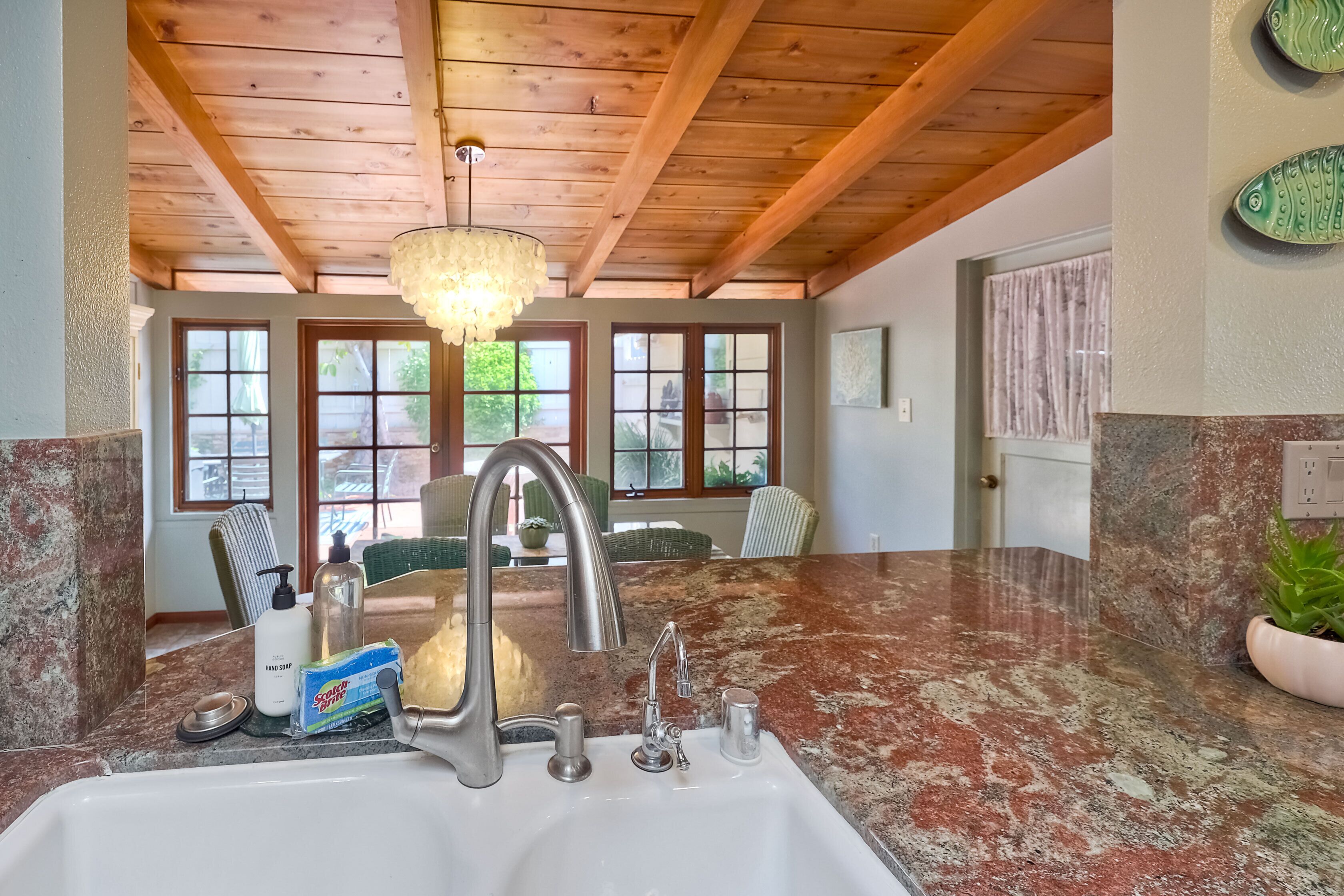 A kitchen with a granite countertop, stainless steel sink, and wooden ceiling beams.