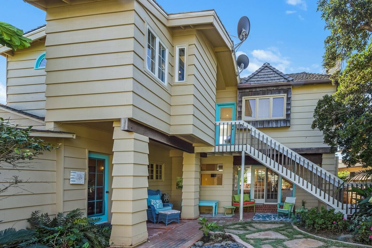 Una casa de dos pisos con un porche cubierto, una escalera y mobiliario exterior.