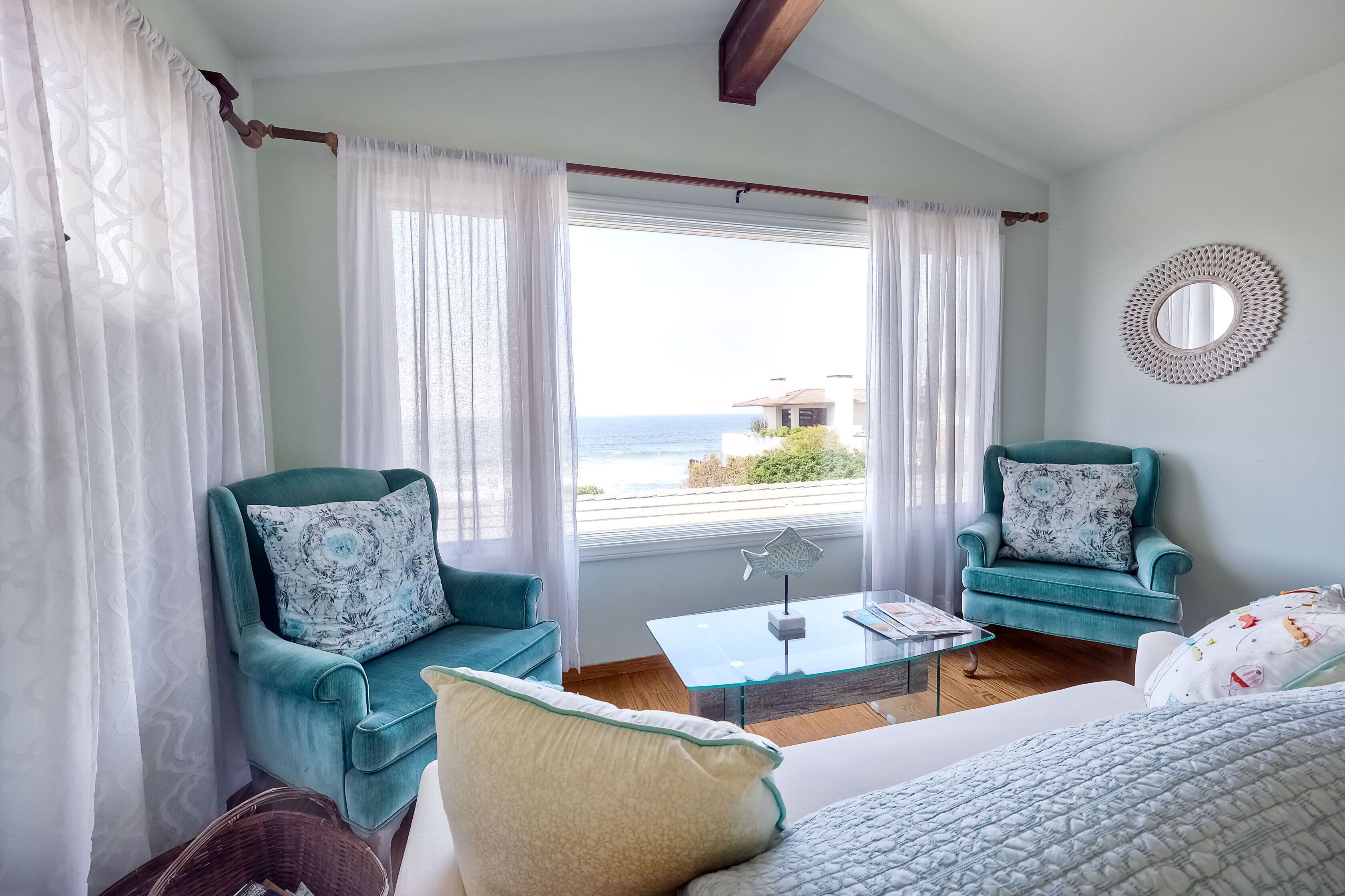 Een kamer met twee smaragdgroene fauteuils, een witte bank en een glazen salontafel, met uitzicht op zee.