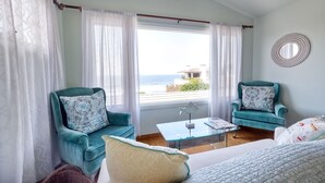 Una habitación con dos sillones azul verdosos, un sofá blanco y una mesa de centro de vidrio, con vista al mar.