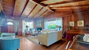 Un amplio salón con pisos de madera y un techo alto, que incluye un sofá, sillones, una mesa de centro y una chimenea.