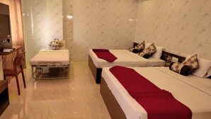 A hotel room with two beds, each with a red blanket, a small table with a chair, and a mirror. - Sri Maharaja Residency (Tiruchirappalli)