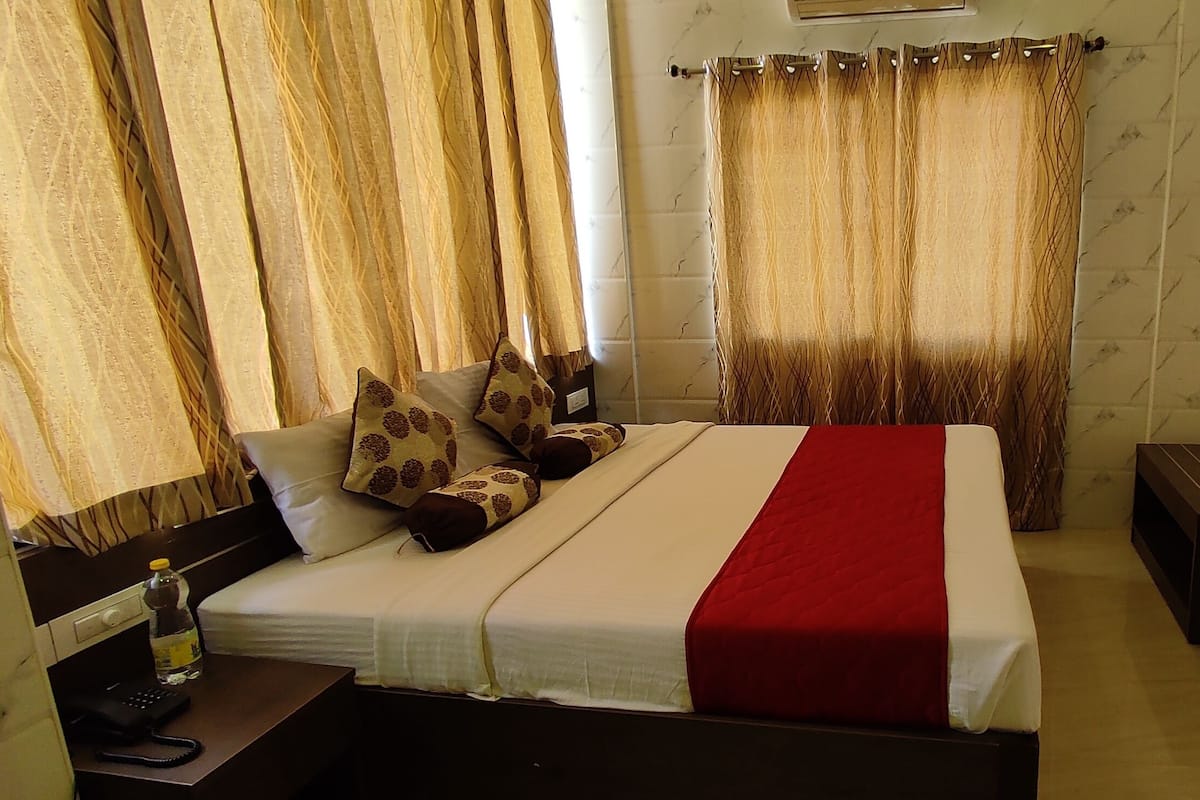 Ein Hotelzimmer mit einem Bett, einem an der Wand befestigten Fernseher, einem Schreibtisch mit Stuhl und Vorhängen.