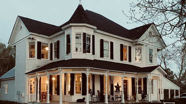 A large, two-story house with a wrap-around porch and a steeply pitched roof.