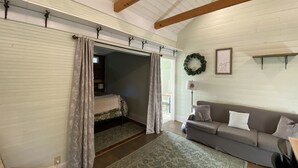 A cozy room with a loft bed, a gray sofa, a patterned rug, and a wooden ceiling.