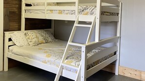A bunk bed with a ladder, wooden beams on the ceiling, and a framed picture on the wall.