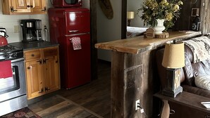 A compact kitchen with wooden cabinets, a red refrigerator, a coffee maker, and a wooden dining table. - Cozy Roscoe Lakefront Cabin (Roscoe)