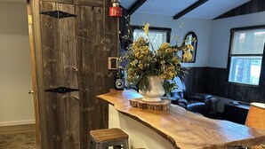 A rustic kitchen with a wooden bar, stools, and a vase with flowers. - Cozy Roscoe Lakefront Cabin (Roscoe)