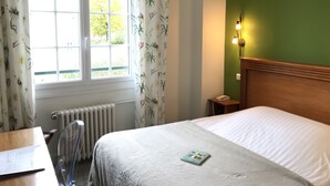 Een hotelkamer met een bed, een bureau, een stoel, een radiator en een raam met gordijnen.
