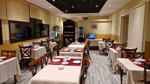 Een restaurant met meerdere tafels, stoelen en een televisiescherm.