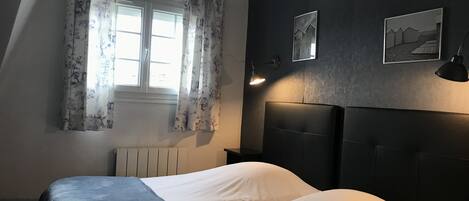 Un dormitorio con dos camas, una ventana con cortinas florales, un radiador y dos lámparas fijadas a la pared.