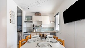 A modern kitchen with white cabinets, a dining table set for four, and a television mounted on the wall.