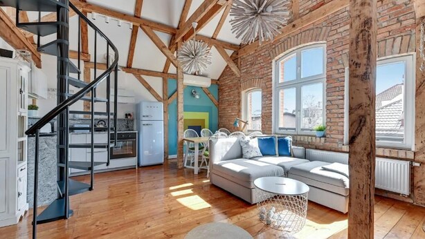 A spacious living area with a wooden floor, a black spiral staircase, a large window with a view, and a cozy seating area with cushions. - Sopot Cosy ATTIC (Sopot)