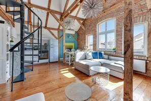 A spacious living area with a wooden floor, a black spiral staircase, a large window with a view, and a cozy seating area with cushions. - Sopot Cosy ATTIC (Sopot)