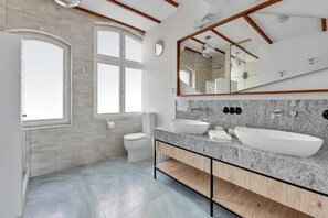 Un baño moderno con un amplio ventanal, un lavamanos blanco y un espejo sobre él.