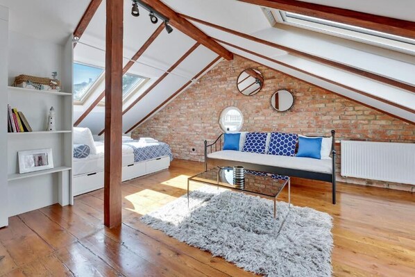 A loft bedroom with a sloped ceiling, exposed brick walls, a white sofa with patterned cushions, a glass coffee table, and a fluffy rug. - Sopot Cosy ATTIC (Sopot)