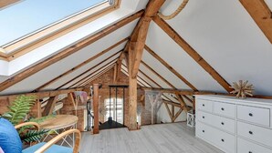 A spacious attic room with exposed wooden beams, a skylight, a white dresser, and a blue chair. - Sopot Cosy ATTIC (Sopot)