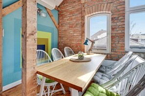 Un comedor con una mesa de madera, sillas blancas, una pared de ladrillo y una ventana.