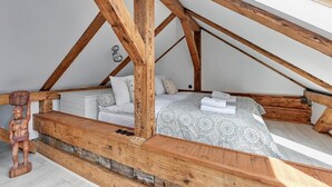 A cozy attic bedroom with a sloped ceiling, wooden beams, a bed with patterned bedding, and a small wooden sculpture. - Sopot Cosy ATTIC (Sopot)
