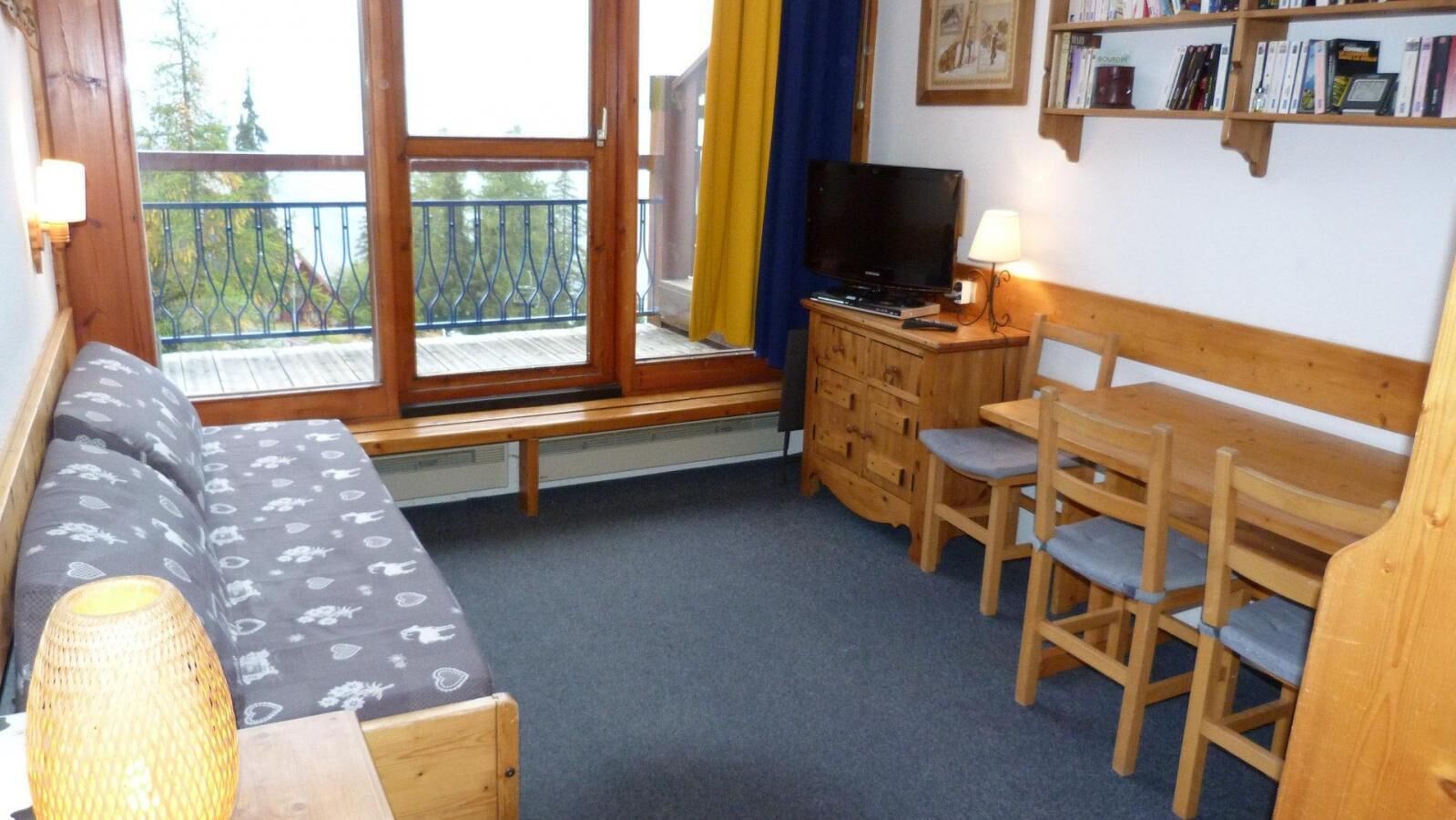 A cozy room with a sofa, a wooden table with chairs, a television, and a bookshelf.