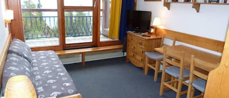 A cozy room with a sofa, a wooden table with chairs, a television, and a bookshelf.