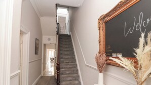 Un pasillo con una escalera, un letrero de bienvenida y un espejo decorativo.