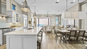A modern kitchen with a large island, white cabinetry, and a dining area with a table and chairs.