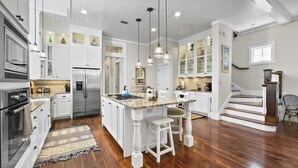 Une cuisine spacieuse avec des meubles blancs, un îlot central et un plancher en bois.