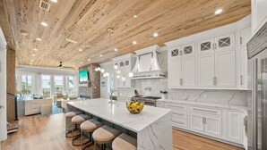 A modern kitchen with a large island, white cabinetry, and a wooden ceiling. - Summer Wind 7 Bedroom Home by RedAwning (Santa Rosa Beach)